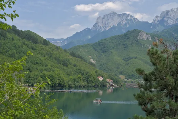 Photo de paysage idyllique d'une voie navigable vers Mostar, avec un bateau et des montagnes.