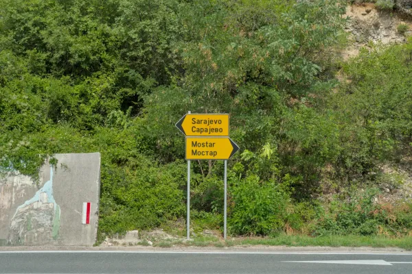 Señal direccional que indica Mostar y Sarajevo entre vegetación verde, marcando una ruta importante.