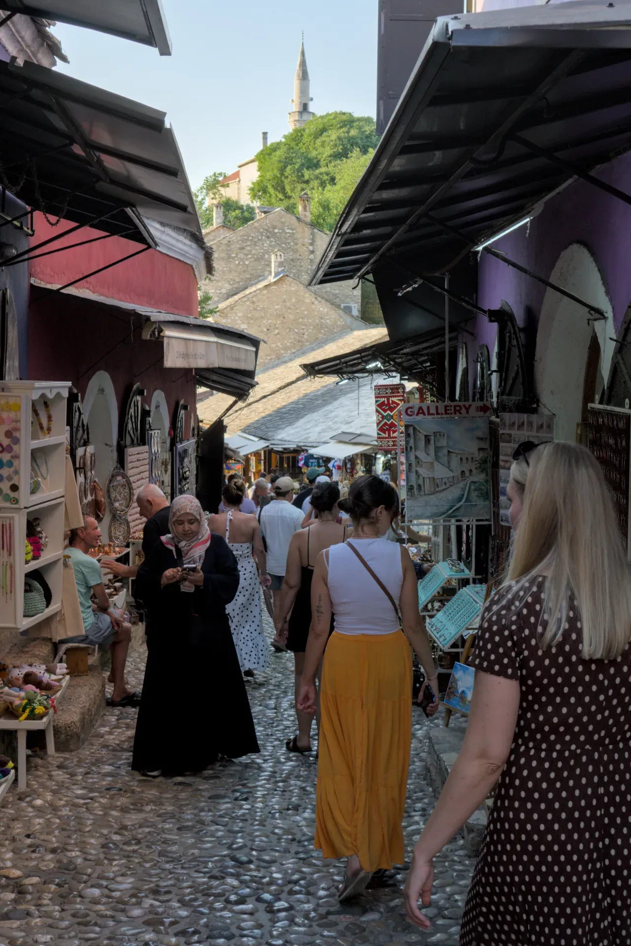 Porträt einer belebten Gasse in Mostars Altstadt am Abend mit Kopfsteinpflaster und historischen Gebäuden.