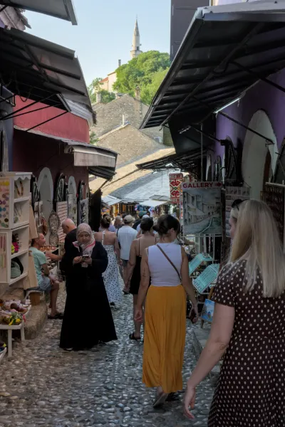 Vista en retrato de un callejón concurrido en el casco antiguo de Mostar al anochecer, con adoquines y arquitectura histórica.