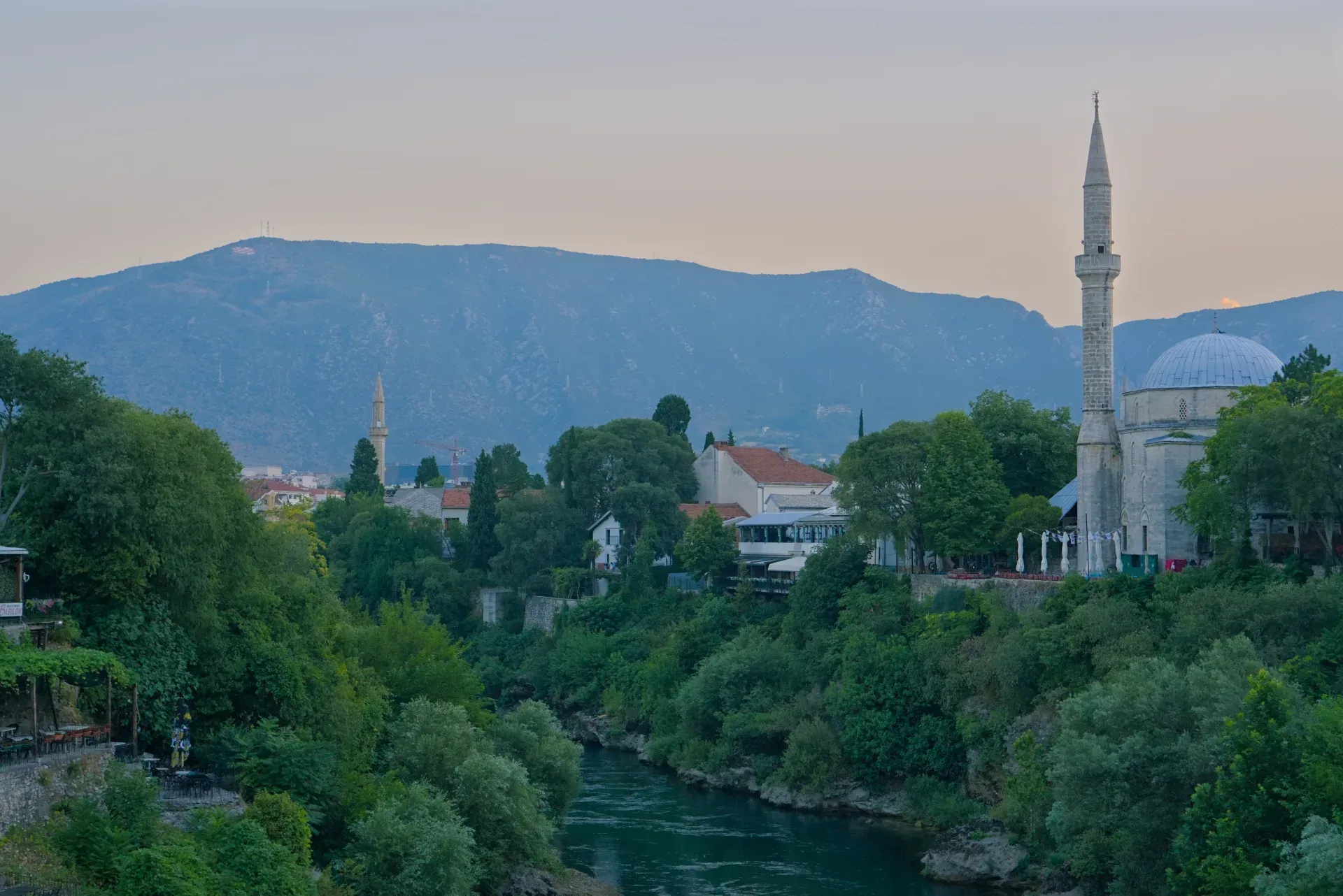 Città vecchia di Mostar prima dell'alba, con il fiume Neretva, vegetazione lussureggiante e una moschea, catturata in orientamento orizzontale.