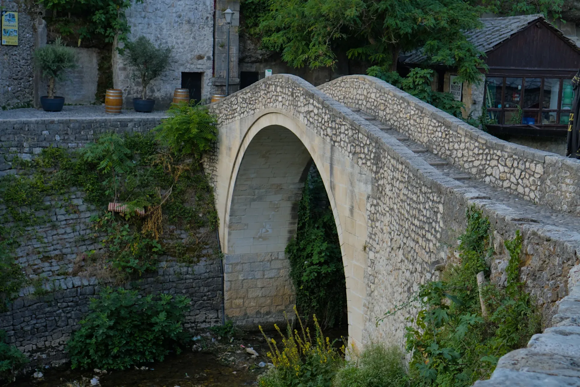 Un ponte di pietra a un solo arco, conosciuto come 'krivi most' o ponte storto, a Mostar, Bosnia ed Erzegovina, circondato da verde.