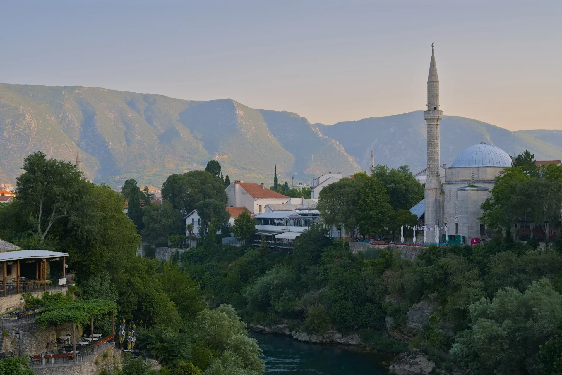 Photographie de paysage de Mostar à l'heure dorée, avec une rivière, une mosquée et des montagnes.