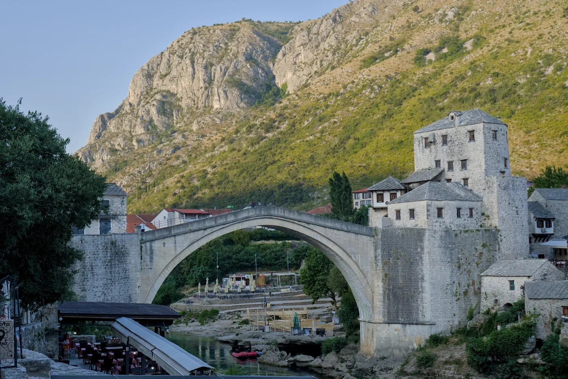 Stari Most u Mostaru u zoru, sa planinskom pozadinom i rekom.