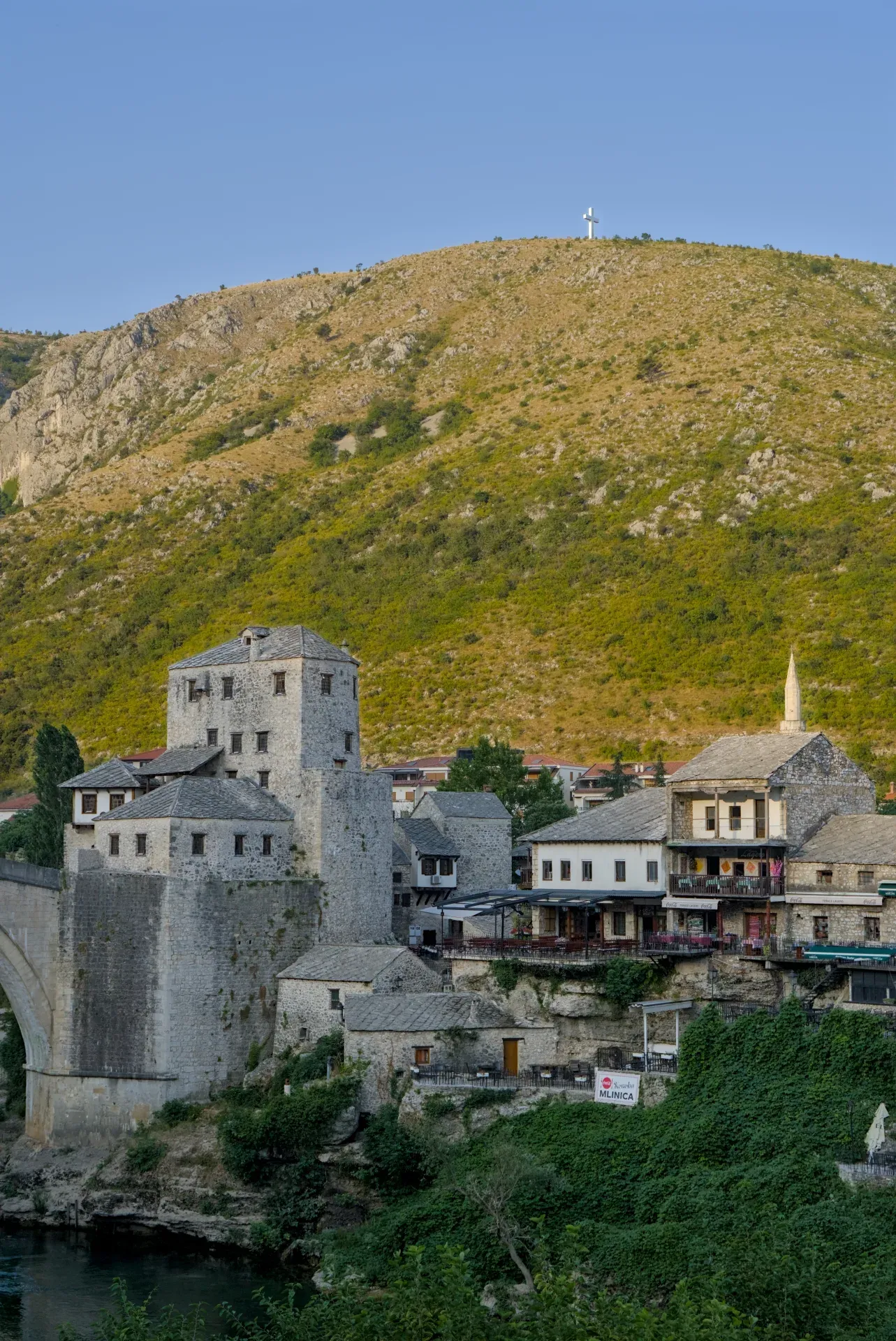 Ora d'oro sulla storica città vecchia di Mostar, con edifici in pietra e una montagna sullo sfondo.