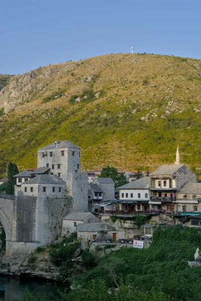 Hora dorada sobre el histórico casco antiguo de Mostar, con edificios de piedra y una montaña al fondo.
