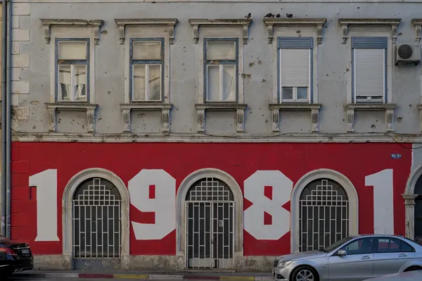 Grafiti "1981" en una pared roja en Mostar, Bosnia y Herzegovina, con ventanas históricas y detalles de fachada.