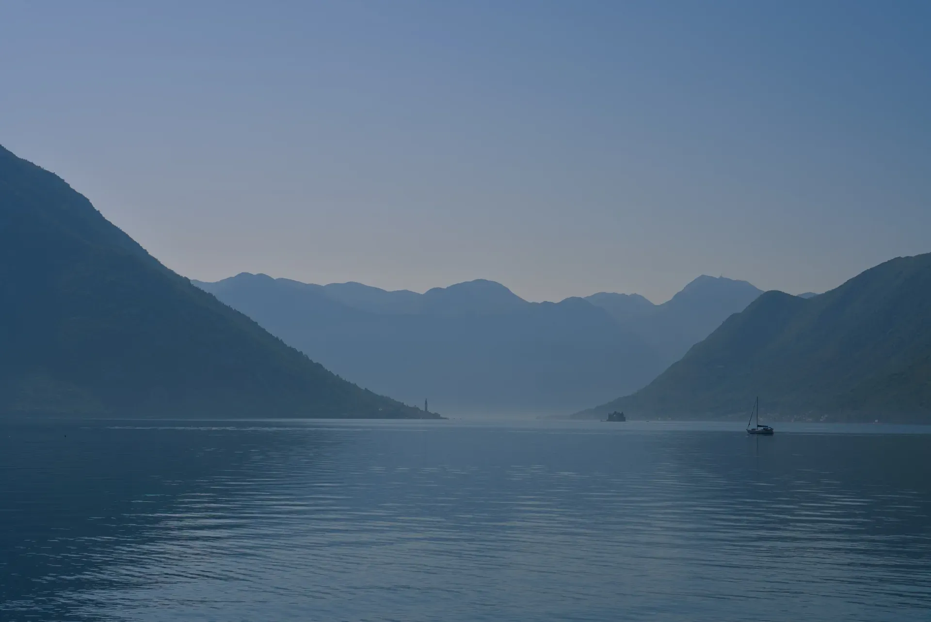 Vue matinale brumeuse de la baie de Kotor, Monténégro, avec montagnes, eau, voilier et vue lointaine de Perast.