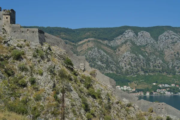Blick vom Berg auf die historischen Festungsmauern von Kotor, Montenegro, mit grünen Hügeln im Hintergrund.