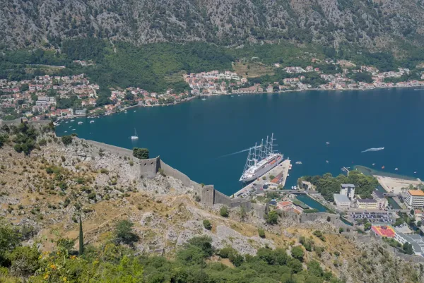 Ein riesiger Segelschoner liegt im Hafen von Kotor, Montenegro, mit historischen Festungsmauern im Vordergrund.