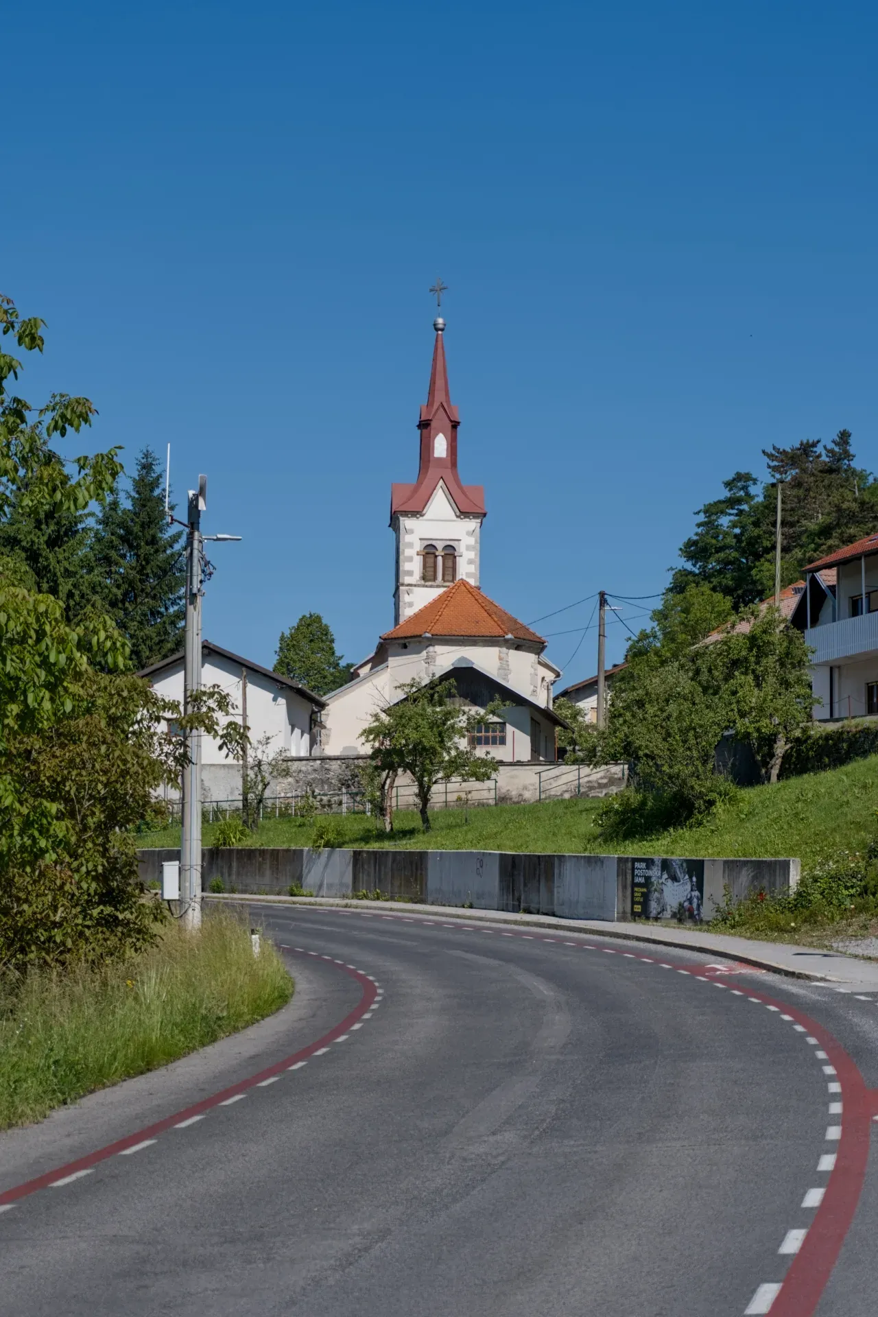 Put vodi ka crkvi sa istaknutim crvenim tornjem u Predjame, Slovenija, pod vedrim plavim nebom.