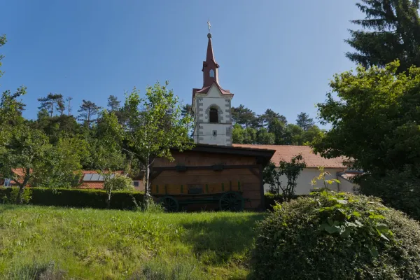 Une église de village pittoresque avec un clocher rouge et une remise en bois avec une vieille charrette, sur la route du Château de Predjama, Slovénie.