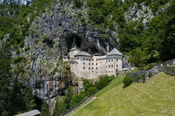 El histórico Castillo de Predjama emerge majestuosamente de un acantilado vertical en Eslovenia, rodeado de exuberante vegetación.