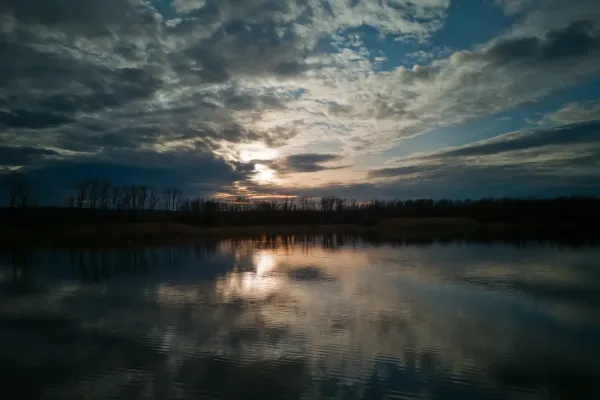 Atardecer dramático sobre el agua en Begečka Jama cerca de Novi Sad, mostrando nubes y reflejos.