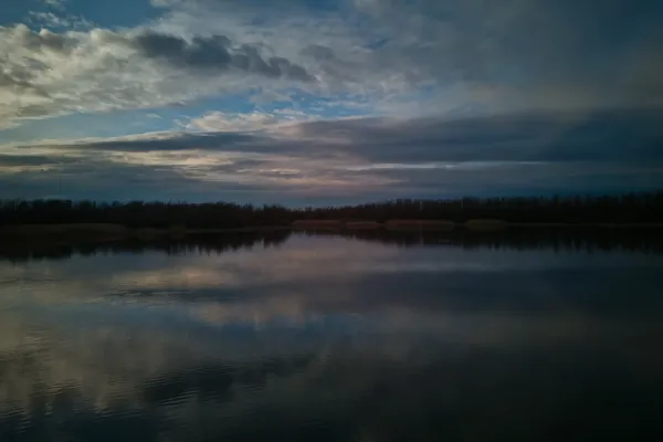 Begečka Jama antes del atardecer, con nubes dramáticas reflejadas en la superficie del agua tranquila.