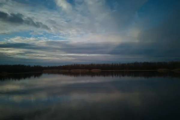 Fotografía artística de paisaje de Begečka Jama en Serbia, mostrando un cielo dramático y reflejo en el agua.
