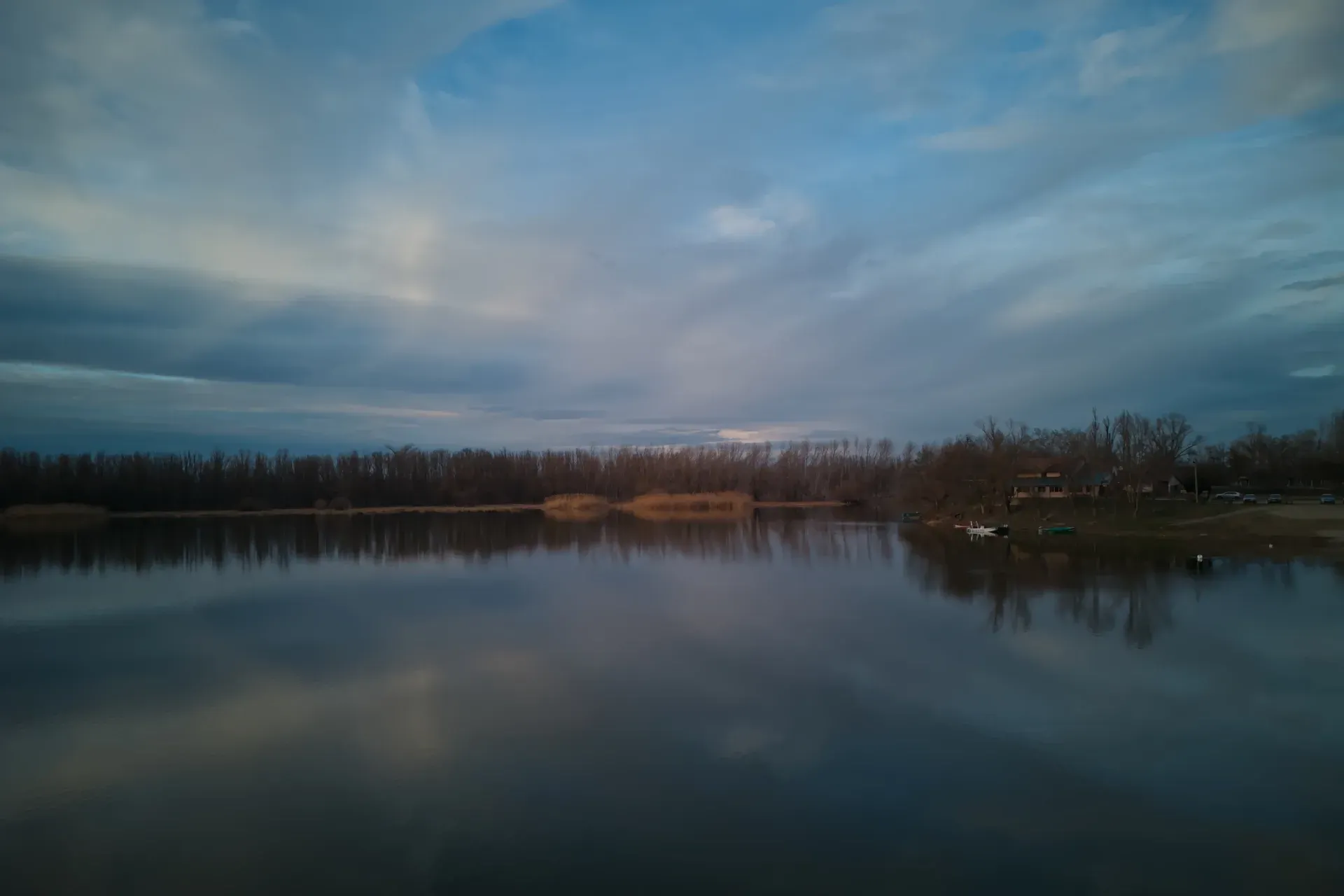 Ruhiger See mit Spiegelung des Himmels und Bäumen am Ufer, Novi Sad