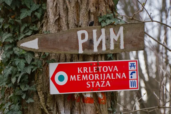 Ein Holzwegweiser mit der Aufschrift "Рим" und einem roten Schild mit der Beschriftung "Krletova Memorijalna Staza" auf einem Baum in der Fruska Gora.