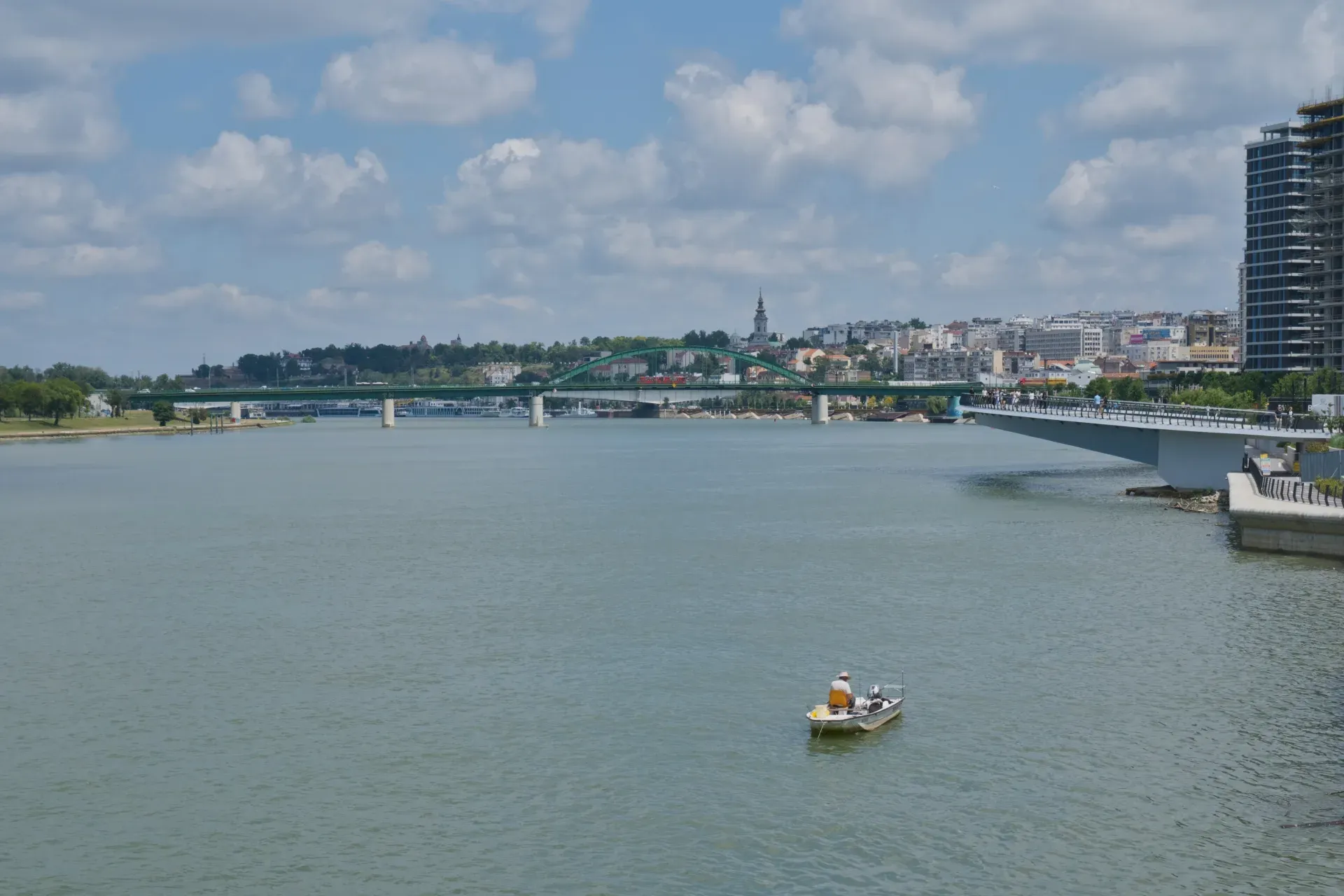Ein einsamer Fischer in einem Boot auf der Save mit Blick auf die Brücken und die Stadtlandschaft von Belgrad.