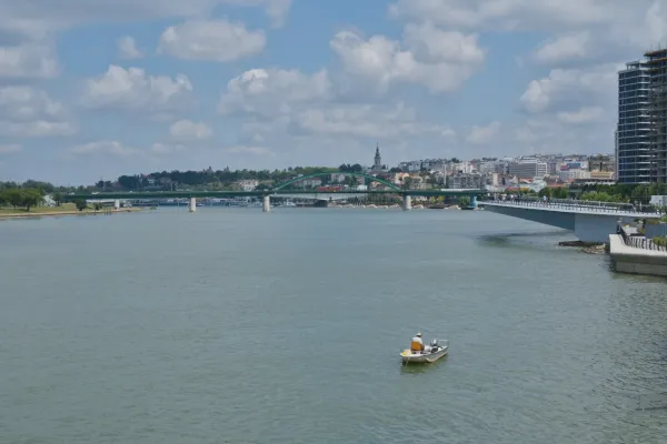 Ein einsamer Fischer in einem Boot auf der Save mit Blick auf die Brücken und die Stadtlandschaft von Belgrad.