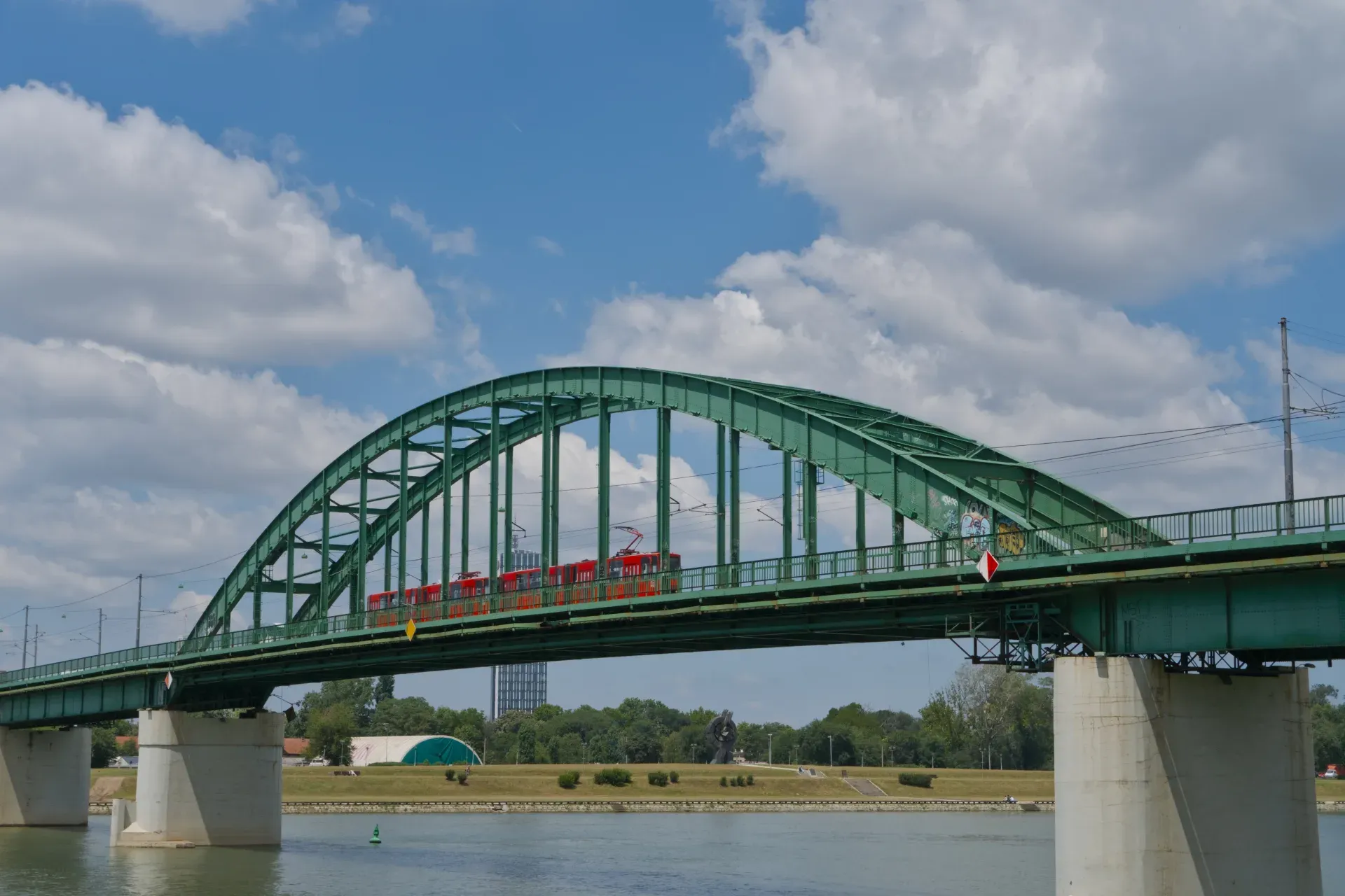 Il Vecchio Ponte Sava a Belgrado con un tram rosso che lo attraversa su uno sfondo blu cielo.