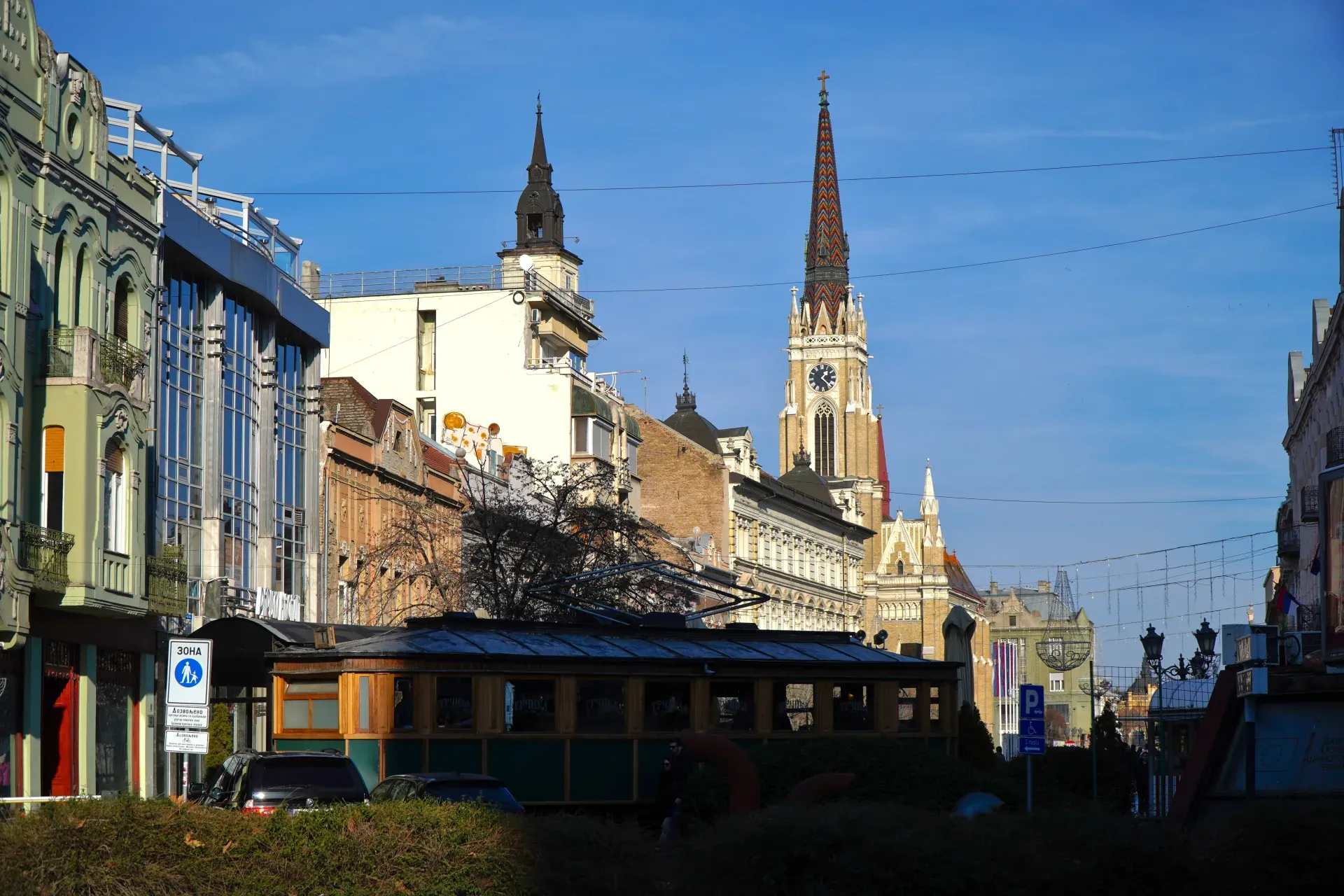 Blick auf den Freiheitsplatz von der Željeznička Straße in Novi Sad, Serbien, mit einer Straßenbahn und einer Kirche.