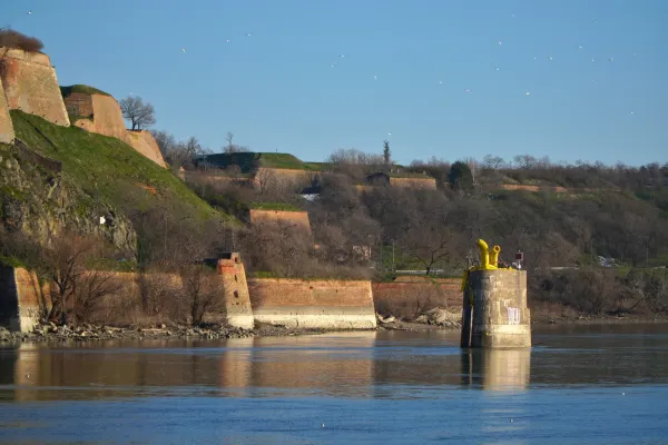 Muros de piedra de la Fortaleza de Petrovaradin se elevan sobre las aguas azules del Danubio bajo un cielo despejado, creando un paisaje histórico.