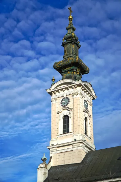 Turm der St. Georgskirche in Novi Sad mit Uhr vor blauem Himmel mit Wolken.