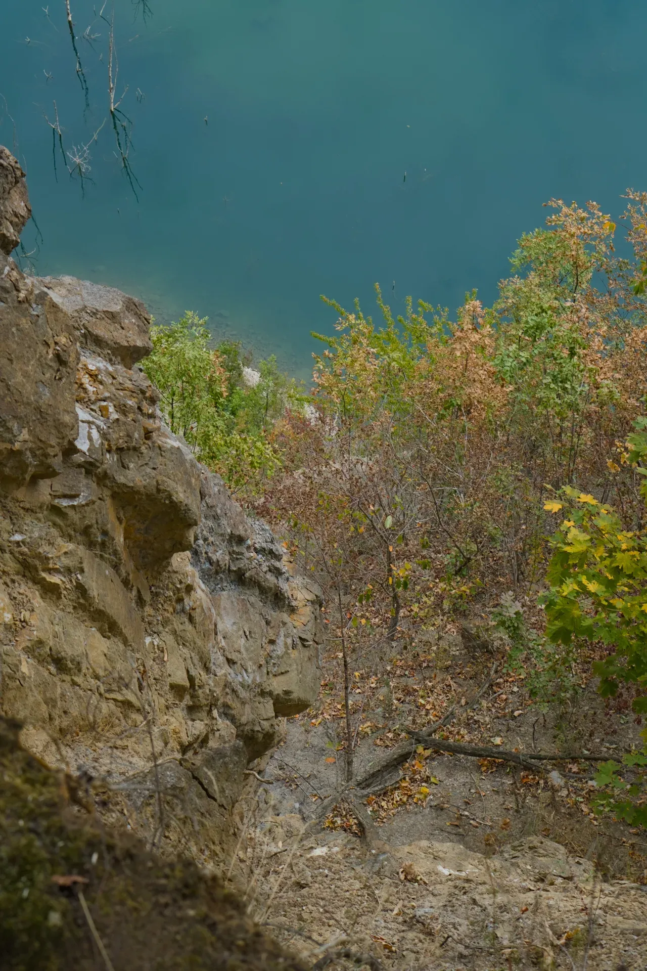Blick von einer hohen, steilen Klippe auf den Ledinačko See, Serbien, mit türkisfarbenem Wasser und Herbstbäumen.