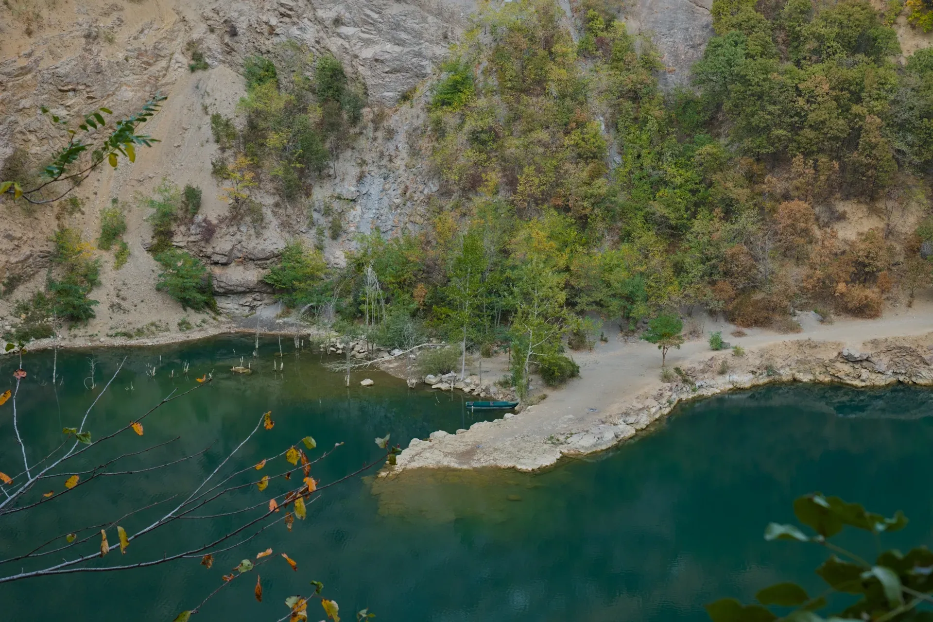 Petit bateau près de la rive rocheuse du lac Ledinačko, entouré d'arbres et de rochers.