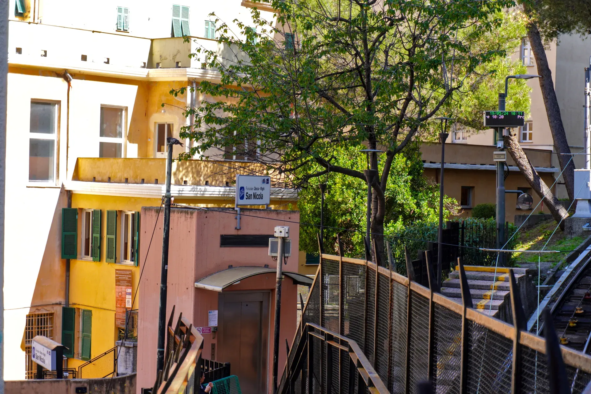 Vue de la gare de la Funicolare San Nicola à Gênes, Italie, avec une façade de couleur pêche, un ascenseur moderne et une signalisation pour la Funicolare Zecca – Righi.