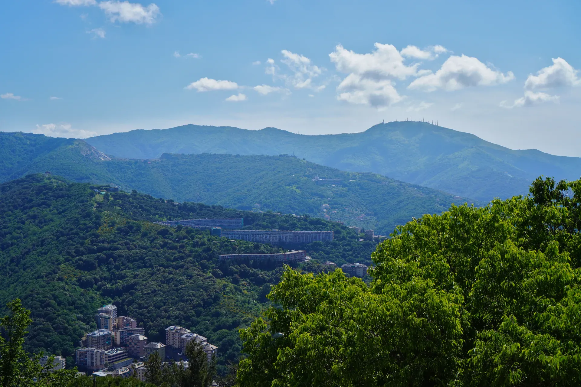 View of green hills near Genoa, Italy, with a village and a modern concrete viaduct.