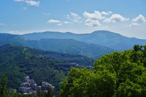 Pogled na zelene brežuljke u blizini Đenove, Italija, sa selom i modernim betonskim vijaduktom.