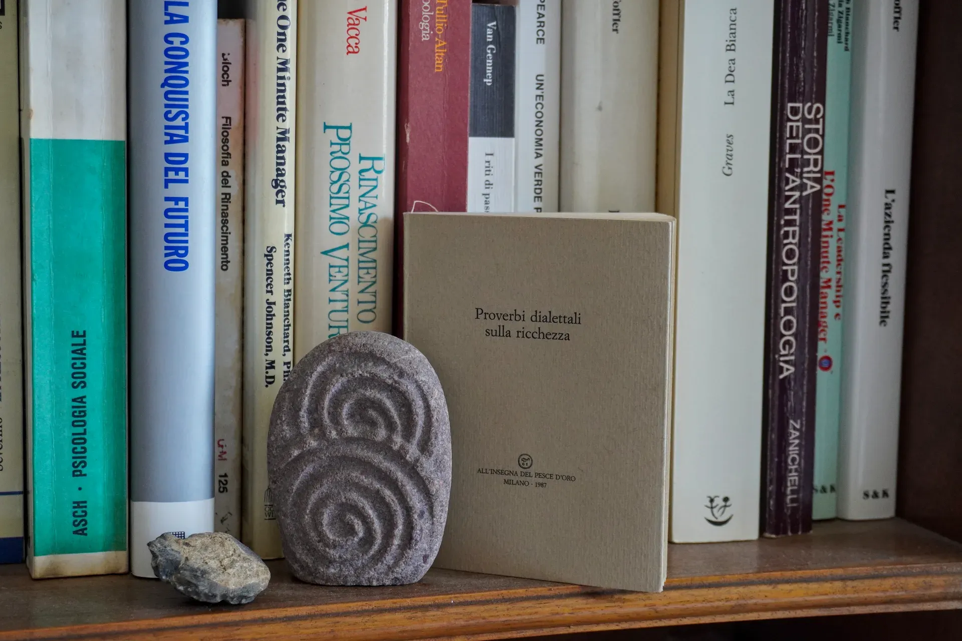 Une étagère à livres à Gênes, Italie, présentant une variété de livres italiens et un objet en pierre sculptée.