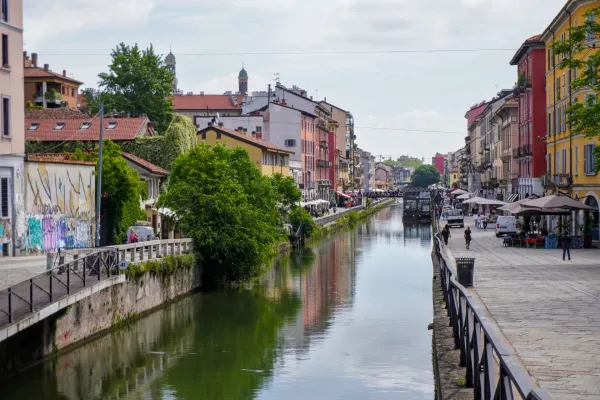 Un canal dans le quartier Navigli de Milan présentant des bâtiments colorés, une structure flottante appelée 'Square Garden', un bateau et un scooter.