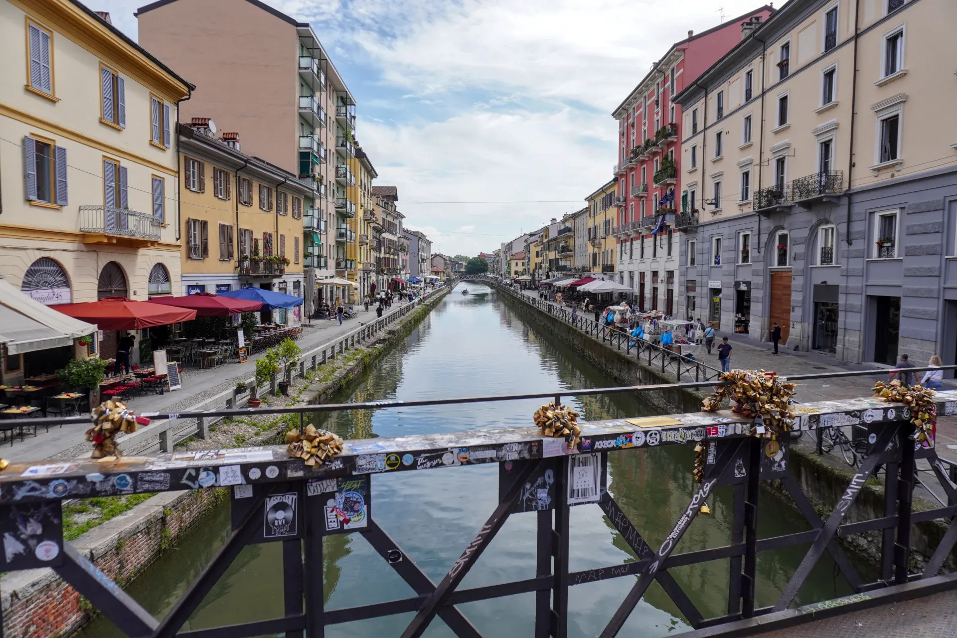 Persone che remano in barca su un canale fiancheggiato da edifici storici e ristoranti all'aperto nel quartiere Navigli di Milano.