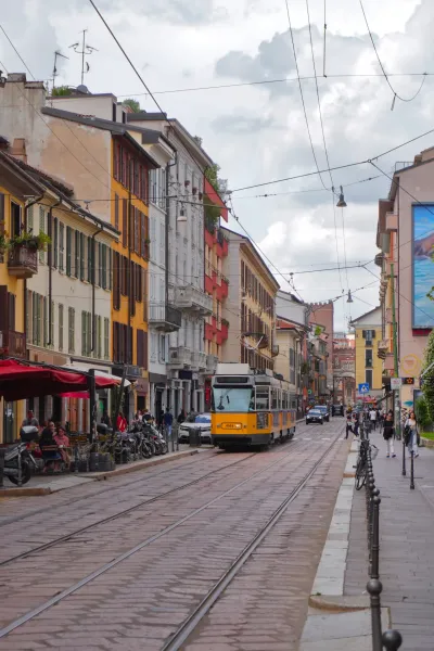 Une rue à Milan, Italie, avec des pavés, des rails de tramway et des bâtiments des deux côtés. Une arche en briques est visible à l'arrière-plan.