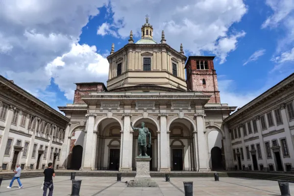 Facade of the Basilica di San Lorenzo Maggiore in Milan, Italy, with a statue of a Roman emperor and a large dome under a cloudy sky.
