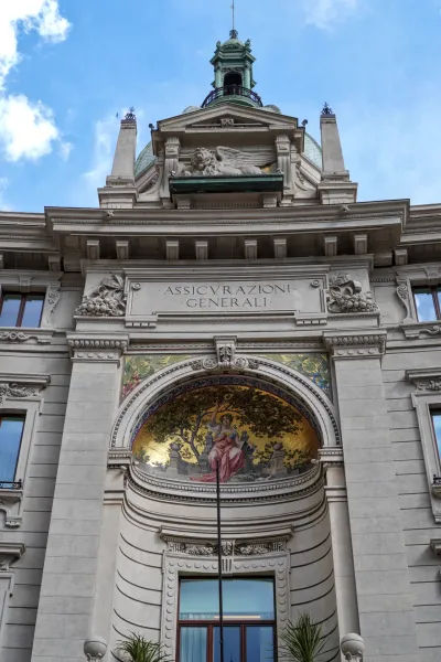 Eine detaillierte Ansicht der oberen Fassade des Gebäudes Assicurazioni Generali in Mailand mit klassischen architektonischen Elementen, einem Mosaik und einem geflügelten Löwen.