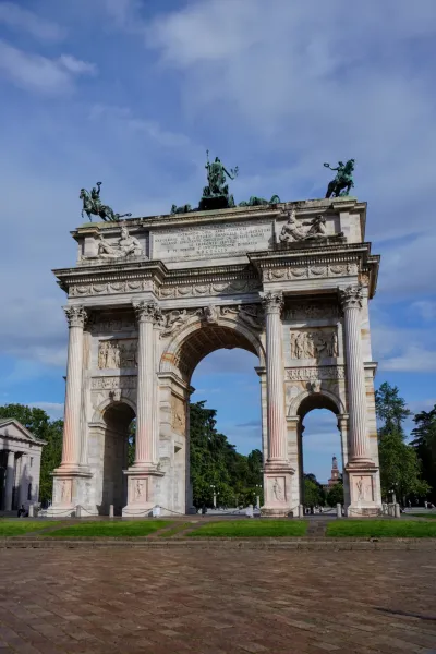 L'Arco della Pace, un grand arc néoclassique, couronné d'une sculpture de quadrige sous un ciel bleu éclatant avec des nuages épars.