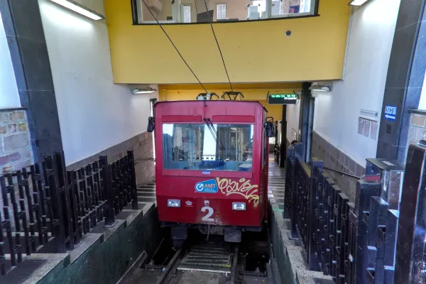 Un tren de funicular rojo está estacionado en una estación con escaleras que conducen a la salida y barreras de tickets en primer plano.