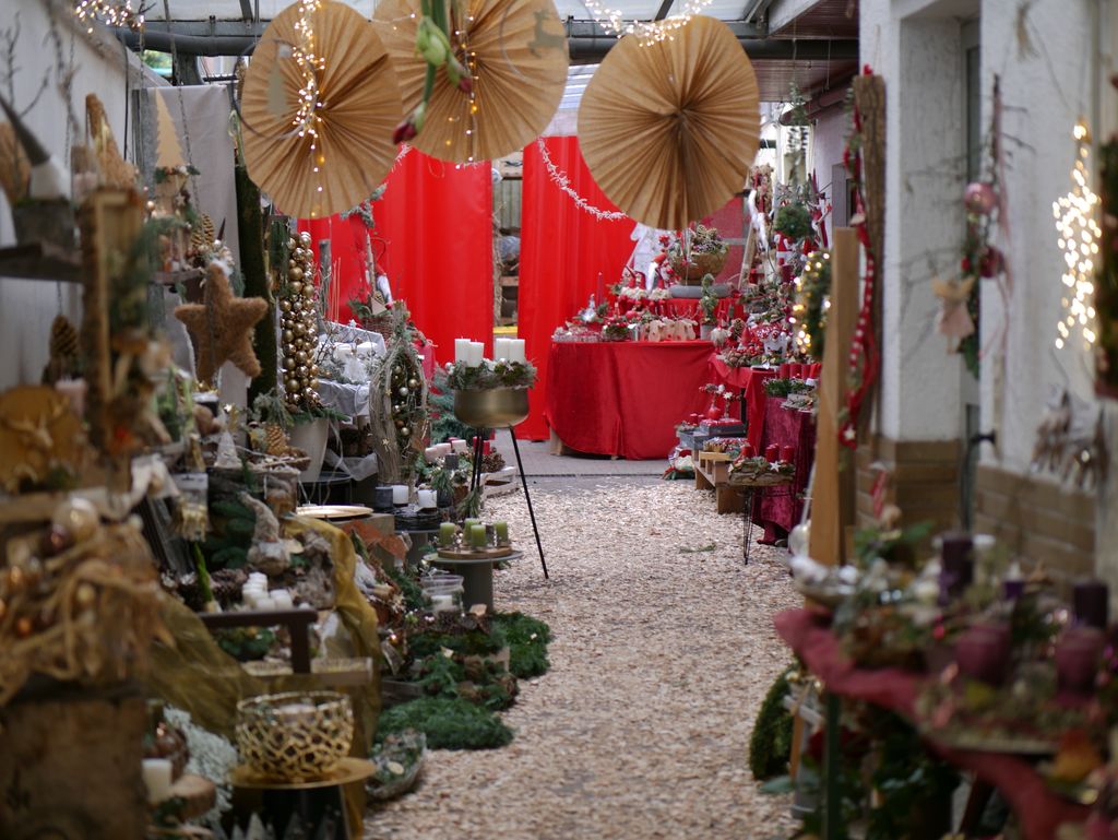 Innenraum eines weihnachtlich dekorierten Geschäfts mit zahlreichen festlichen Dekorationen, Kunsthandwerken und Kerzen auf Tischen und Regalen in einem engen Gang.