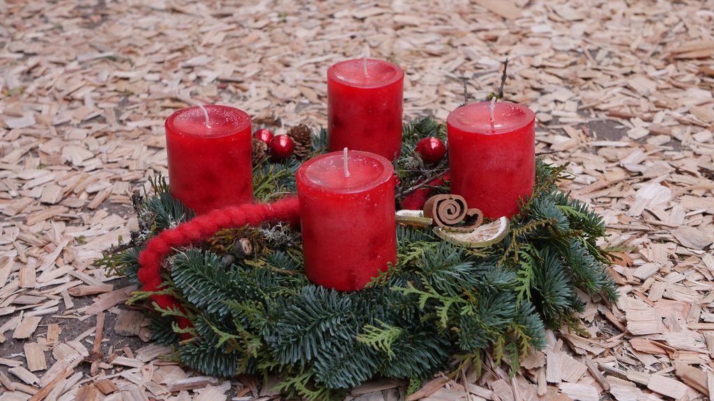 Ein Adventskranz mit vier roten Kerzen und Tannenzweigen steht auf einer mit Holzspänen bedeckten Oberfläche.