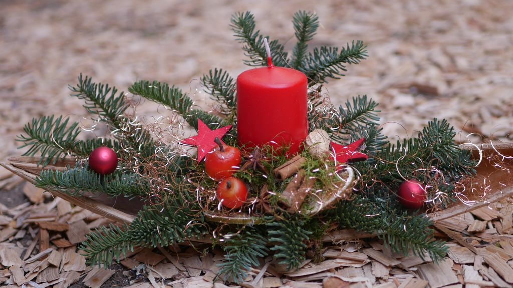 Weihnachtliche Dekoration mit roter Kerze, Tannenzweigen, roten Kugeln, Zimtstangen und roten Sternen auf Holzhackschnitzeln.