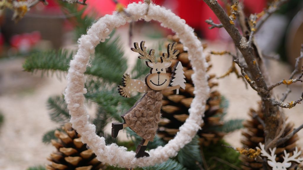 Eine weihnachtliche Dekoration mit einer Rentierfigur, die in einem weißen Ring hängt, umgeben von Tannenzapfen und Tannenzweigen.