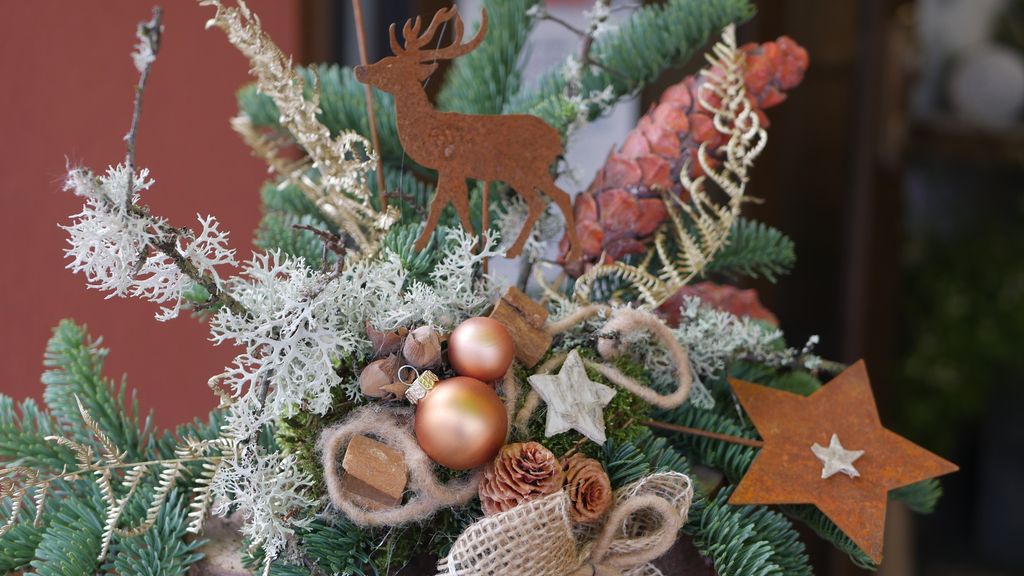 Weihnachtliche Dekoration mit Tannenzweigen, Zapfen, goldenen Kugeln, Sternen und einem Rentier aus Rostmetall.