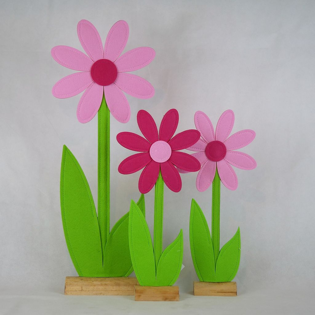Drei bunte Filzblumen mit langen grünen Blättern und Holzsockeln, angeordnet auf weißem Hintergrund.