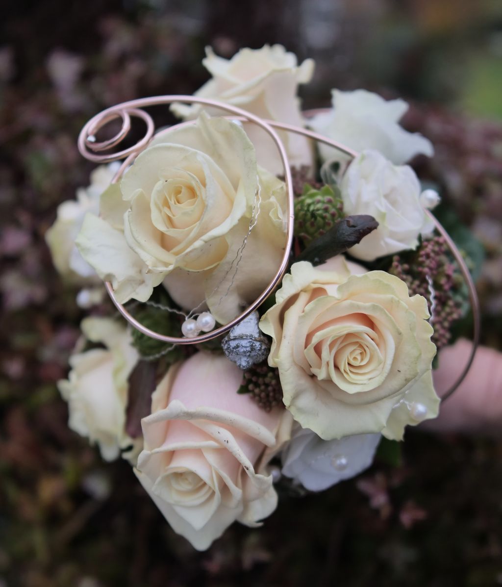 Strauß aus cremefarbenen und weißen Rosen, verziert mit silberfarbenem Draht und kleinen Perlen, aufgenommen vor unscharfem dunklem Hintergrund.