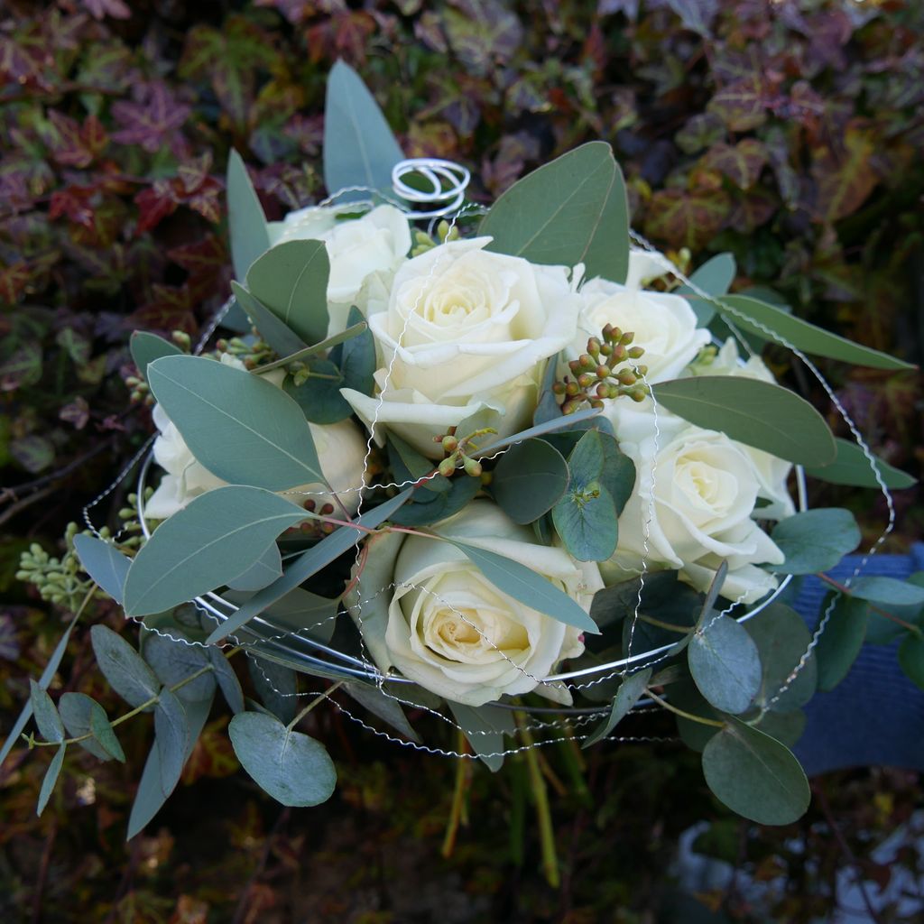 Brautstrauß aus weißen Rosen und Eukalyptusblättern mit Silberdraht, im Freien vor herbstlichem Laub.