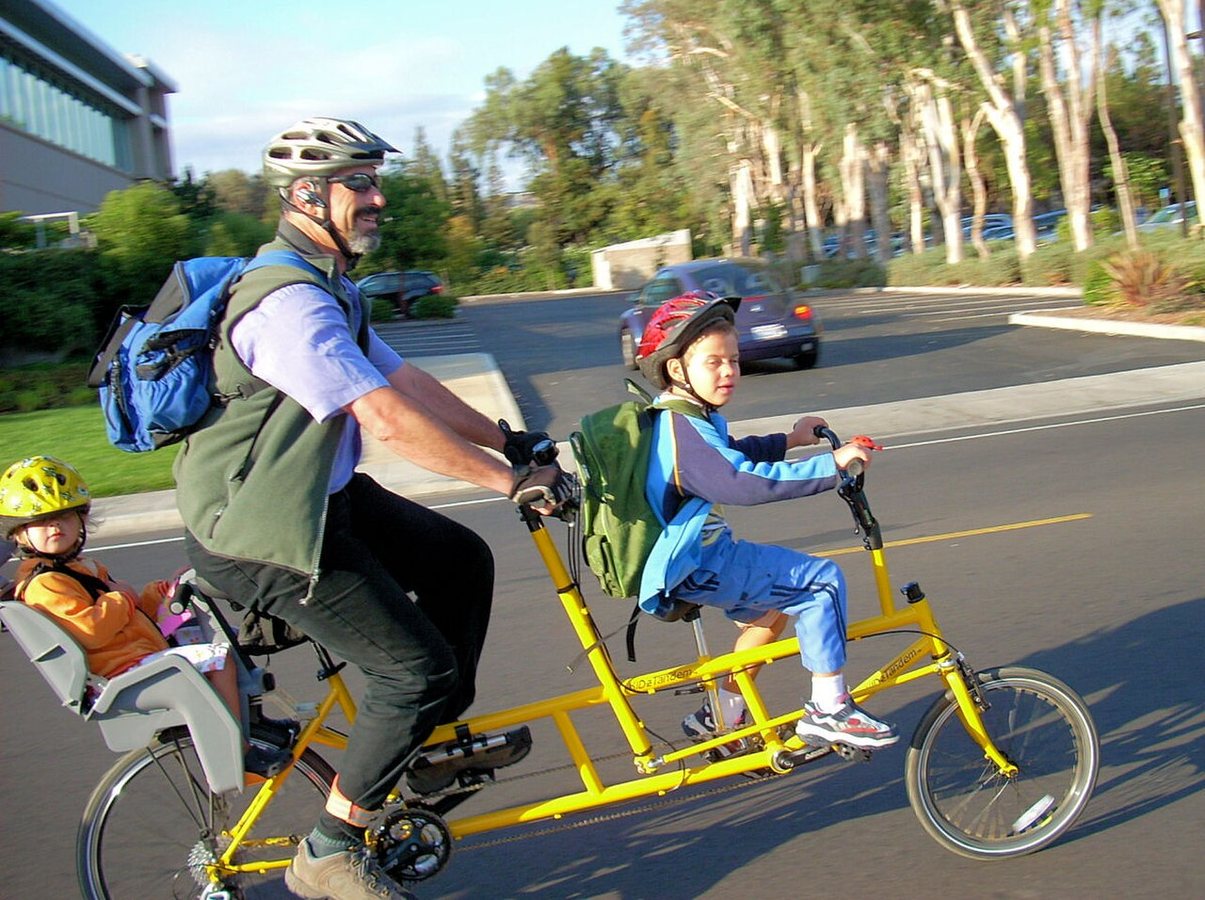 Ein Mann fährt 2007 mit zwei Kindern auf einem mehrsitzigen Fahrrad. In den meisten Industrieländern, mit Ausnahme Frankreichs, verbringen Eltern heute mehr Zeit mit ihren Kindern als früher.